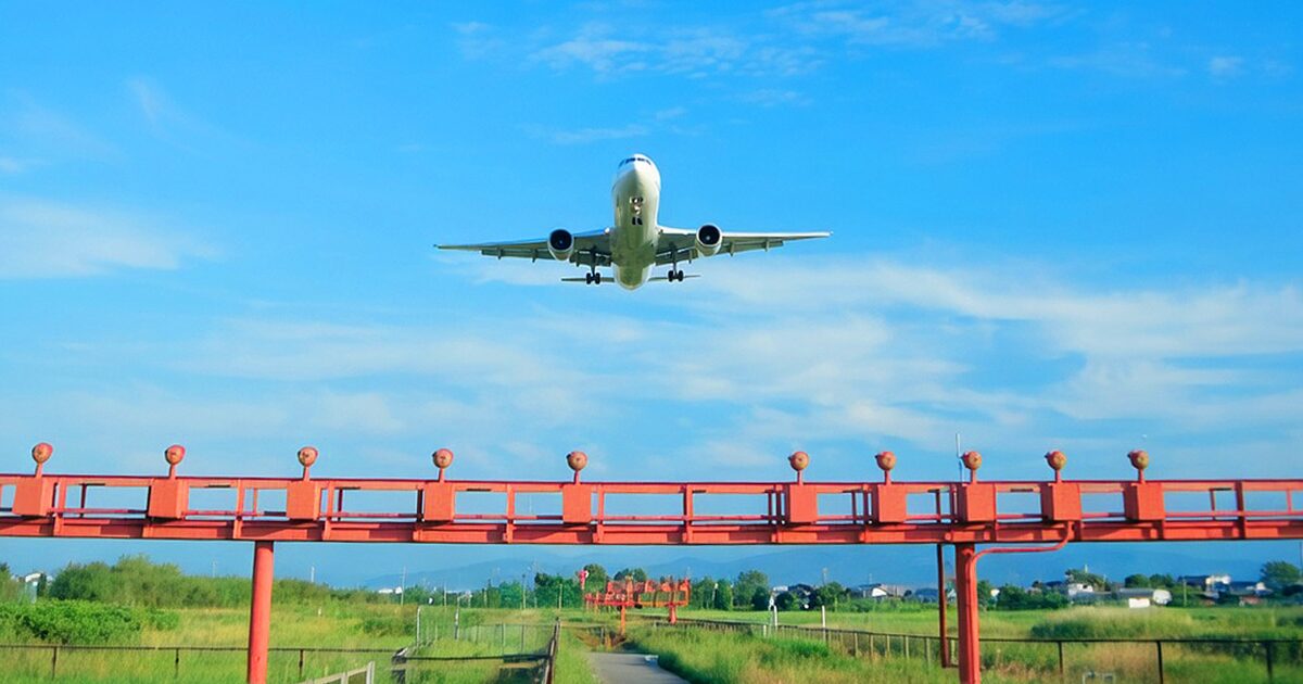 青空の下で進入灯上空を飛行する着陸態勢の旅客機