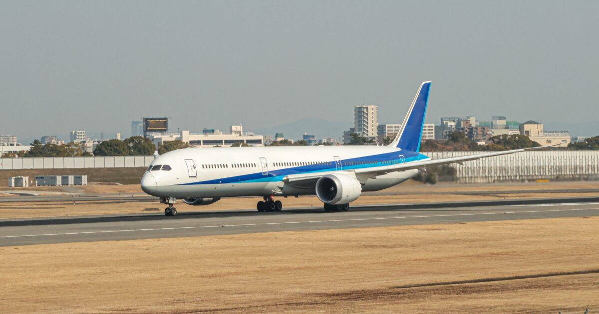 都市を背景に滑走路を走行する青白のジェット旅客機