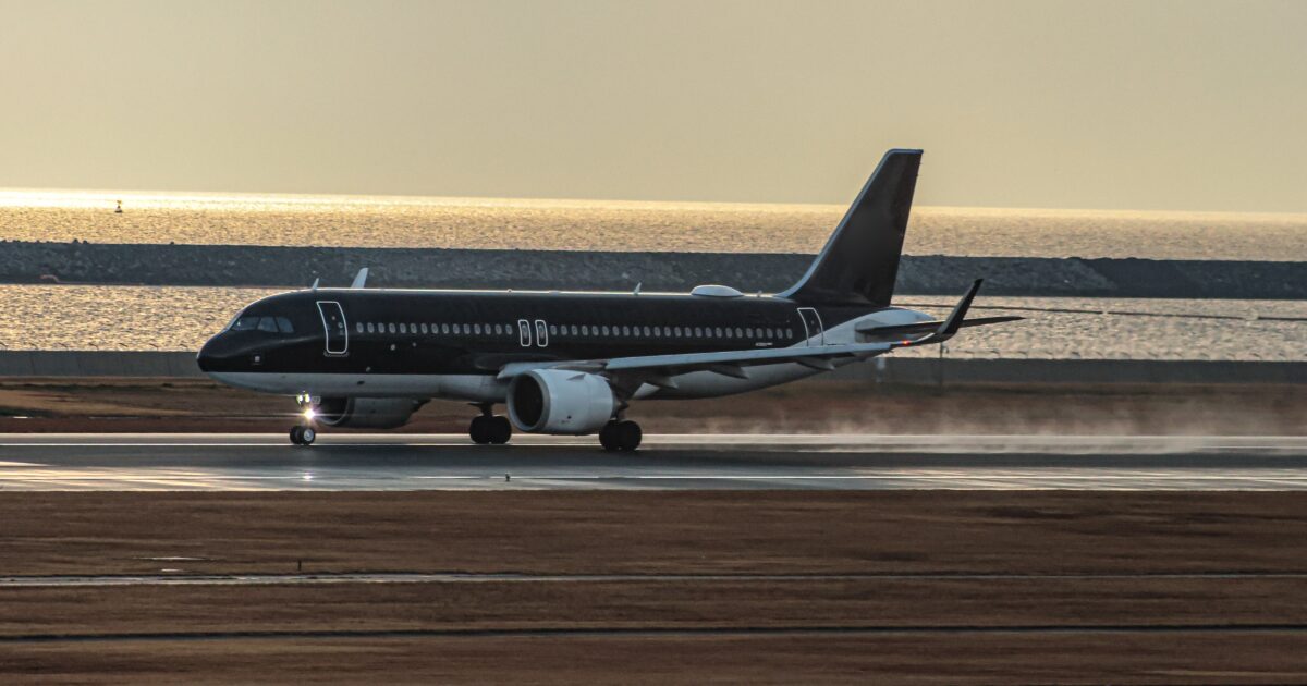 夕暮れの海辺の滑走路に着陸する黒色の旅客機