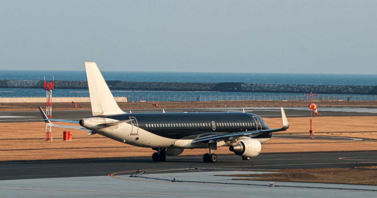 海沿いの空港滑走路を走行する黒塗装のジェット旅客機