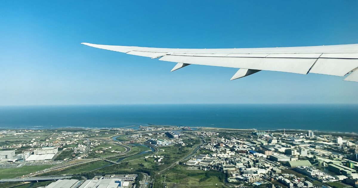 航空機の翼越しに望む海岸線と都市の空撮風景