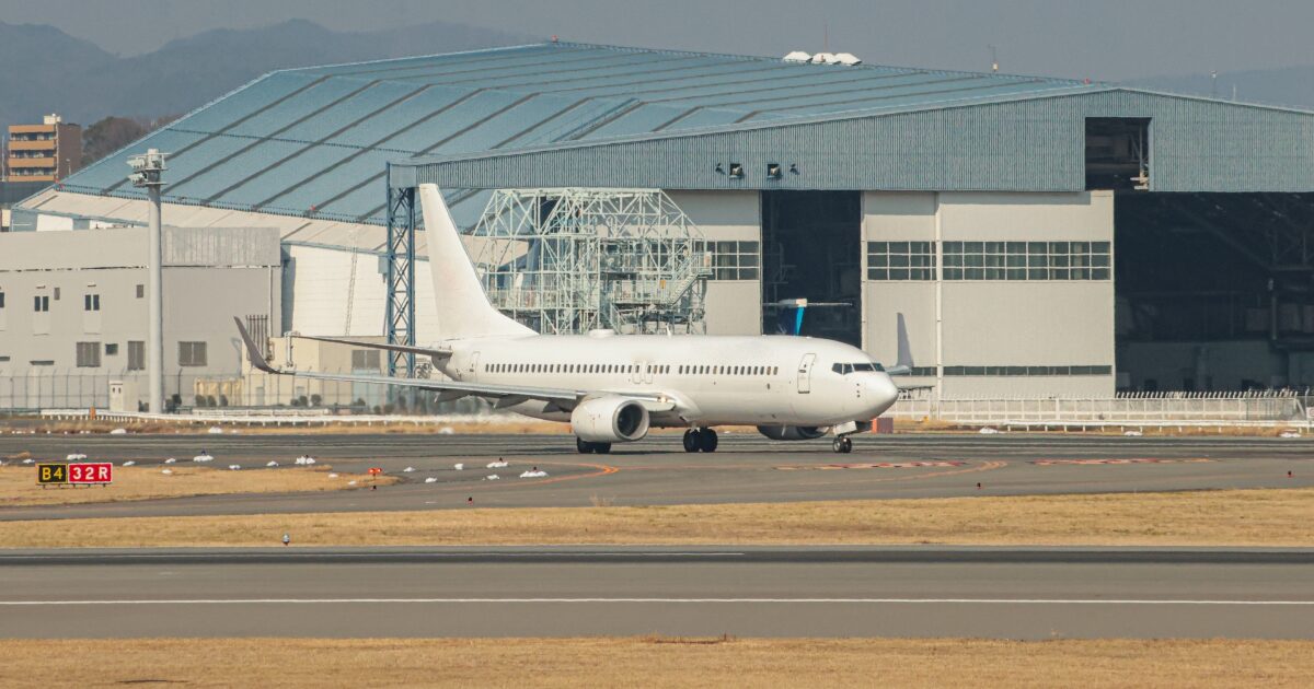 格納庫前の滑走路を走行する白色ジェット旅客機